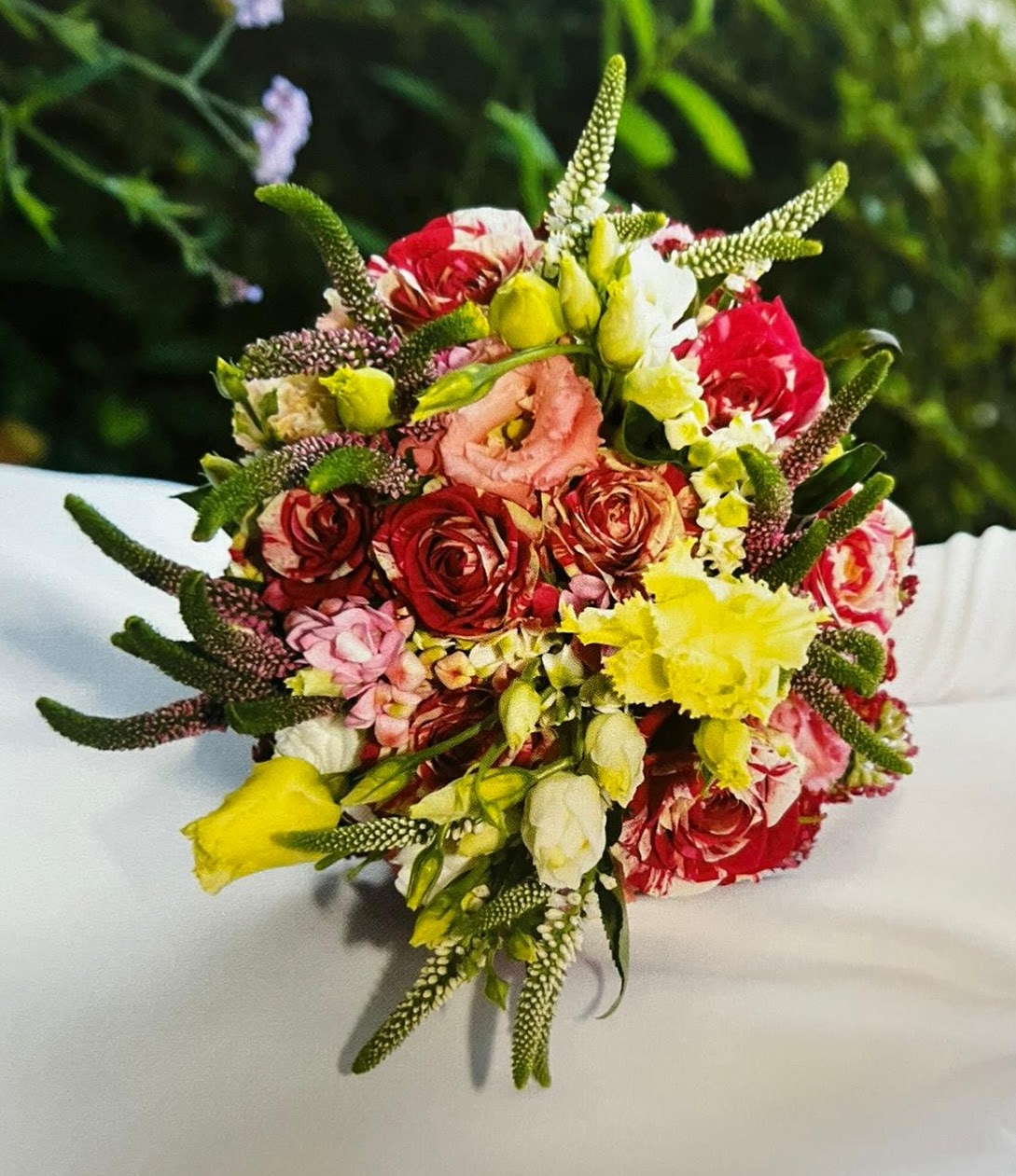 Farbenfroher, runder Brautstrauß mit rot-weiß panaschierten Rosen, pinken und gelben Blüten sowie markanten grünen Veronika-Spitzen.